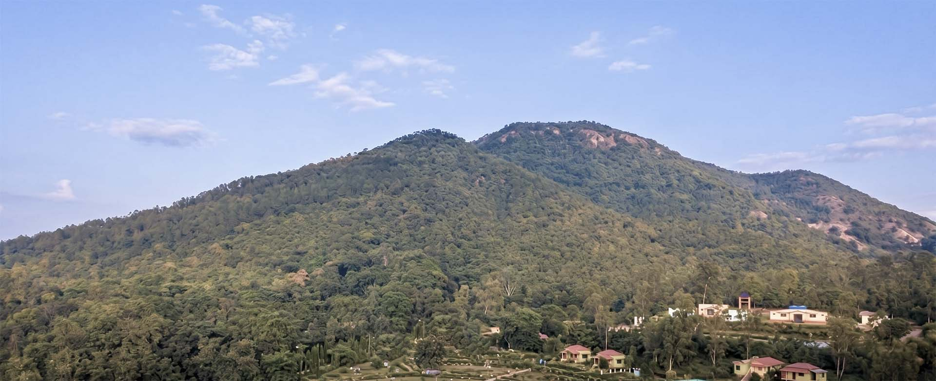 Lush green Susunia Hill under a clear blue sky with small cottages nestled at the base in Bankura, West Bengal.